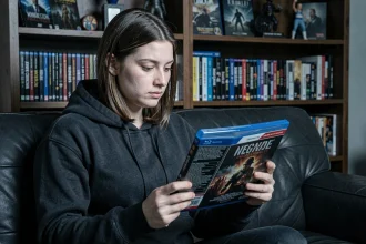 Jeune femme tenant un coffret Blu-ray de film d'horreur et d'action dans un salon avec collection de films